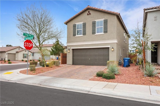 view of front facade with a tiled roof, stucco siding, an attached garage, and decorative driveway