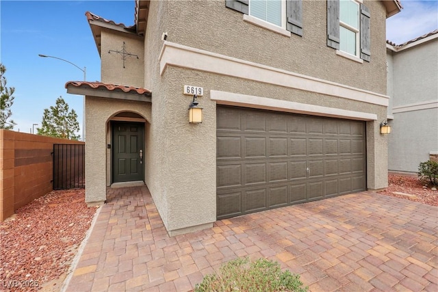 exterior space featuring stucco siding, a tiled roof, an attached garage, and fence