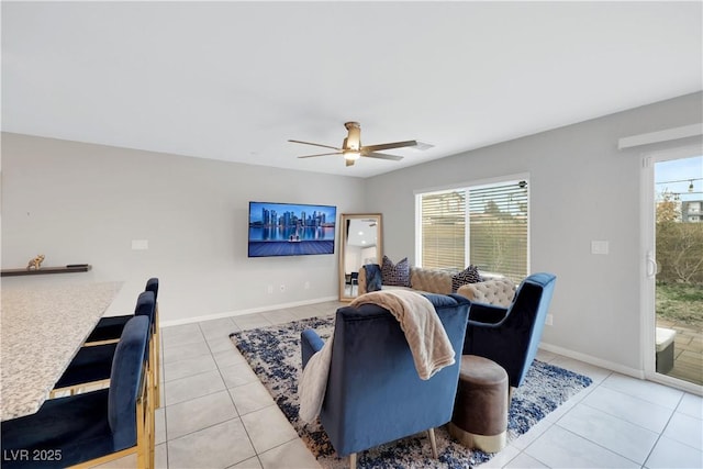 living area featuring a ceiling fan, light tile patterned floors, a healthy amount of sunlight, and baseboards