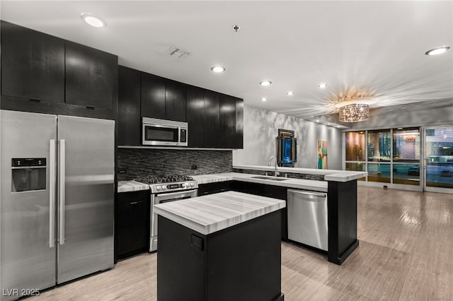 kitchen with light countertops, a peninsula, dark cabinetry, stainless steel appliances, and a sink