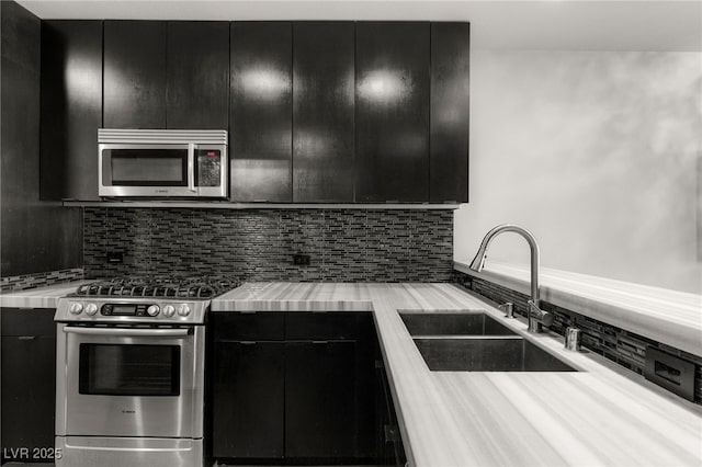 kitchen featuring modern cabinets, a sink, backsplash, dark cabinetry, and appliances with stainless steel finishes