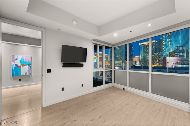 interior space with a tray ceiling, recessed lighting, wood finished floors, and baseboards