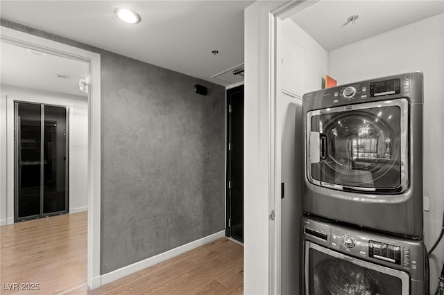 washroom featuring baseboards, stacked washer and dryer, wood finished floors, and laundry area