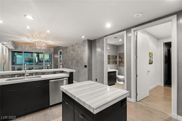 kitchen with a sink, stainless steel dishwasher, dark cabinetry, and light countertops