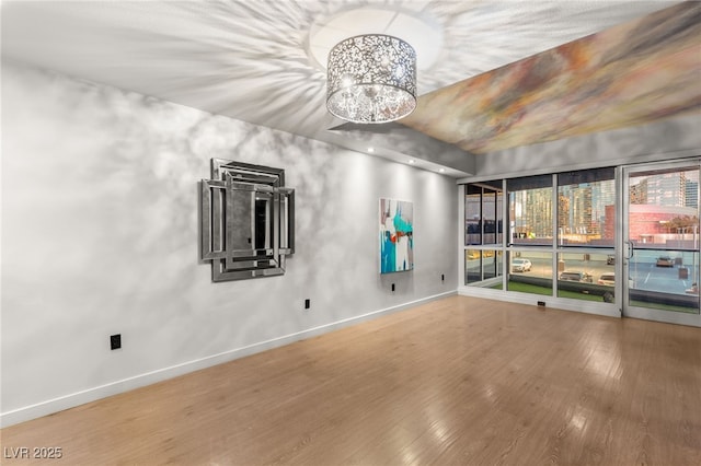 empty room with wood finished floors, baseboards, and a chandelier