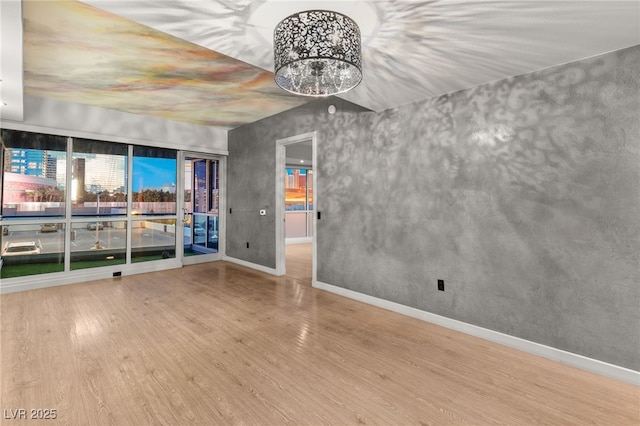 empty room with an inviting chandelier, baseboards, and wood finished floors