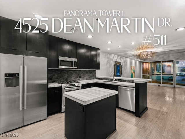 kitchen featuring appliances with stainless steel finishes, dark cabinetry, a sink, light countertops, and a center island