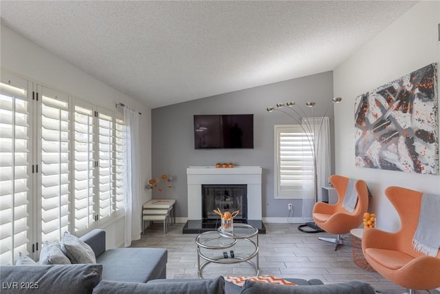 living room featuring baseboards, wood tiled floor, vaulted ceiling, a glass covered fireplace, and a textured ceiling