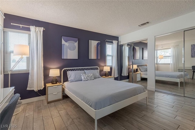 bedroom with visible vents, wood finished floors, multiple closets, and a textured ceiling