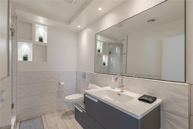 bathroom with vanity, a shower with shower door, recessed lighting, tile walls, and toilet