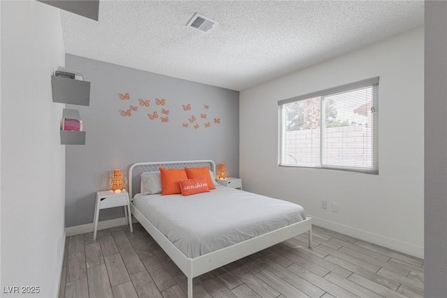 bedroom featuring visible vents, a textured ceiling, baseboards, and wood finished floors