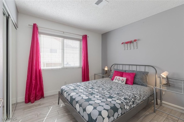 bedroom featuring visible vents, a textured ceiling, wood finished floors, a closet, and baseboards