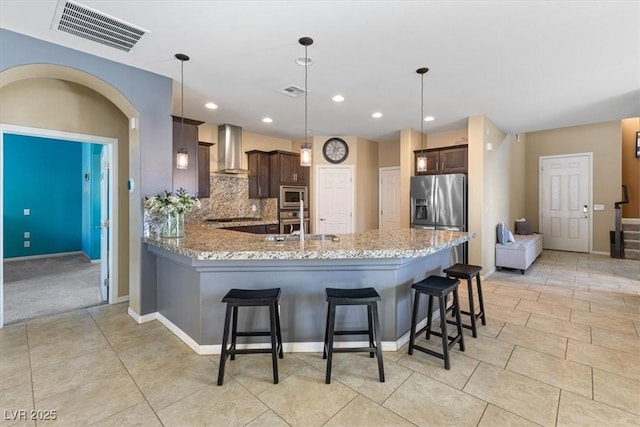 kitchen with dark brown cabinetry, wall chimney exhaust hood, visible vents, and stainless steel appliances