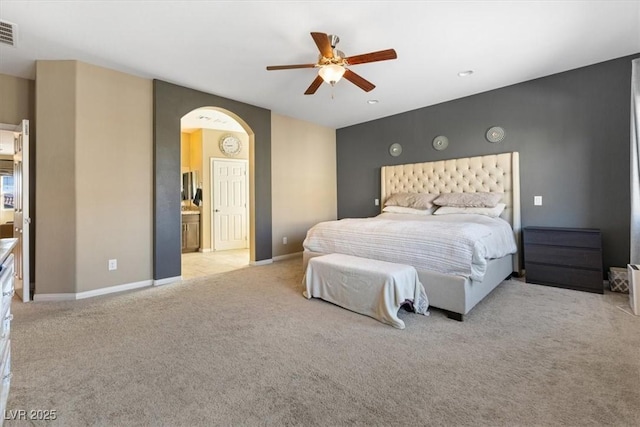 carpeted bedroom featuring a ceiling fan, visible vents, baseboards, ensuite bath, and arched walkways