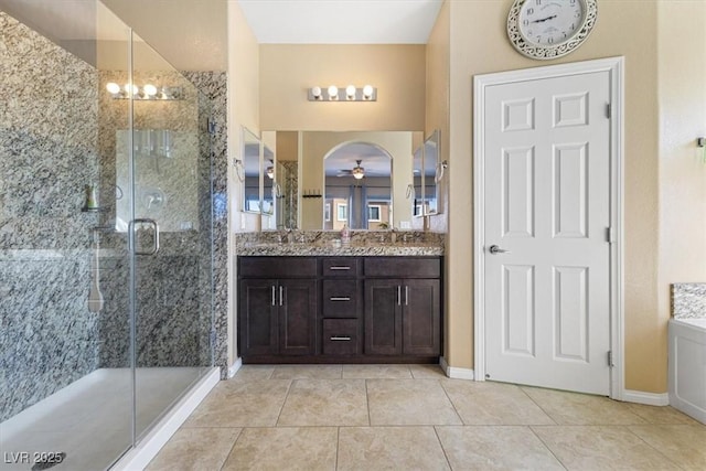 bathroom with a shower stall, double vanity, tile patterned floors, a ceiling fan, and a sink