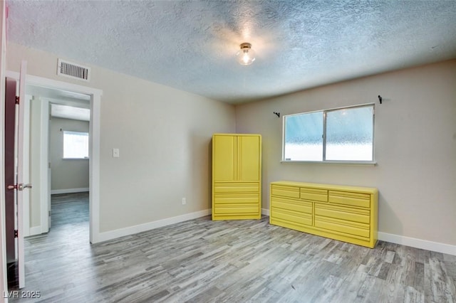 unfurnished bedroom with light wood finished floors, visible vents, a textured ceiling, and baseboards