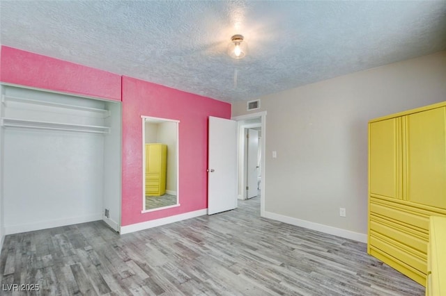 unfurnished bedroom featuring a textured ceiling, wood finished floors, visible vents, and baseboards