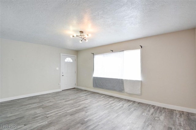 interior space featuring baseboards, a textured ceiling, an inviting chandelier, and wood finished floors