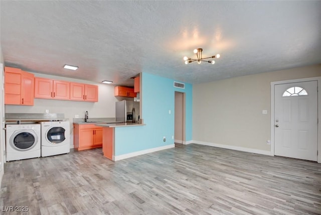 kitchen with light wood-type flooring, stainless steel refrigerator with ice dispenser, washer and dryer, a sink, and a chandelier