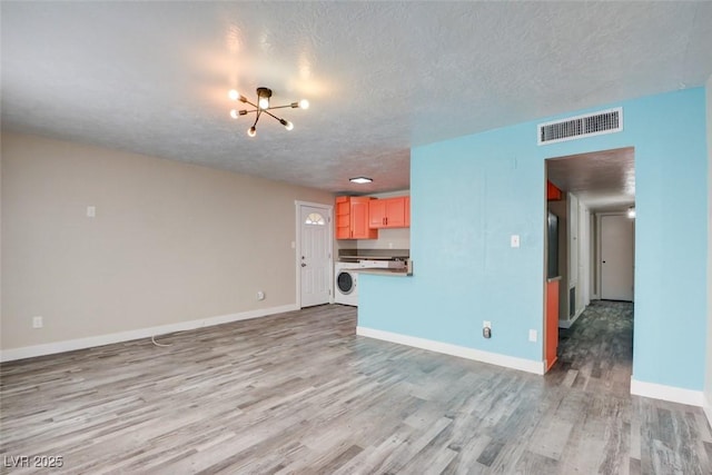 unfurnished living room with baseboards, visible vents, an inviting chandelier, washer / dryer, and light wood-type flooring