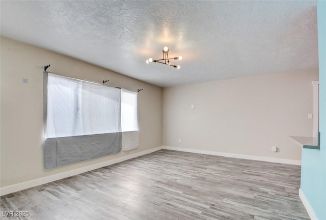 spare room featuring baseboards, wood finished floors, a textured ceiling, and a chandelier