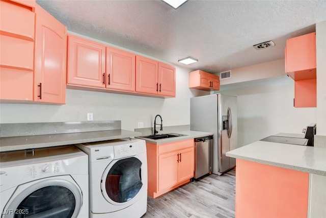 laundry room featuring visible vents, a sink, a textured ceiling, light wood finished floors, and washing machine and clothes dryer