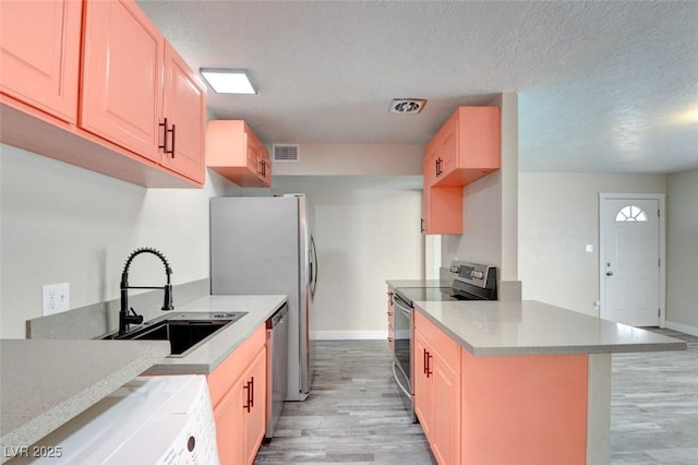 kitchen featuring visible vents, a sink, stainless steel appliances, light wood finished floors, and washer / dryer