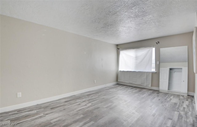 spare room with a textured ceiling, baseboards, and wood finished floors