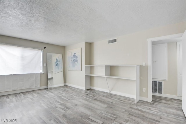 unfurnished living room with wood finished floors, visible vents, and baseboards