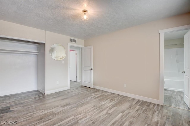 unfurnished bedroom featuring visible vents, a textured ceiling, wood finished floors, a closet, and baseboards