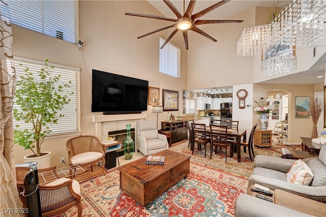 living room with a tiled fireplace, arched walkways, a towering ceiling, and ceiling fan