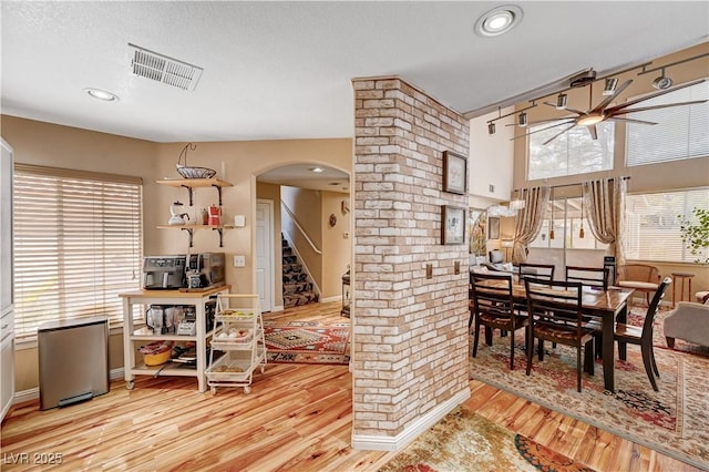 dining room featuring visible vents, a ceiling fan, wood finished floors, arched walkways, and stairs