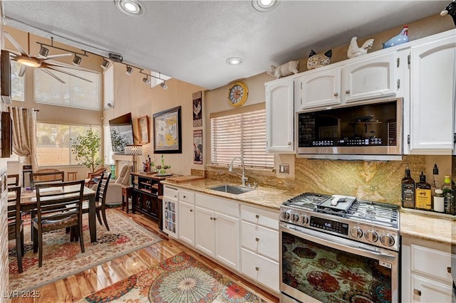 kitchen featuring a sink, light wood-style floors, appliances with stainless steel finishes, white cabinets, and lofted ceiling