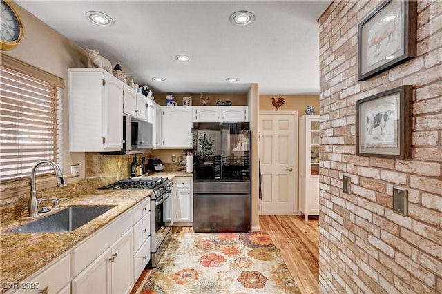 kitchen with a sink, stainless steel appliances, light stone countertops, and white cabinetry