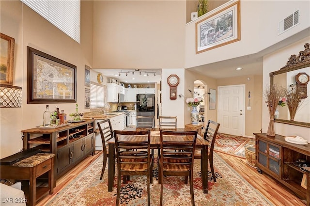 dining area with visible vents, arched walkways, a high ceiling, and light wood finished floors