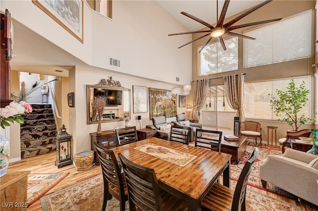 dining room featuring visible vents, stairway, wood finished floors, high vaulted ceiling, and a ceiling fan