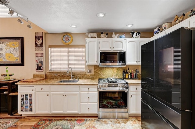 kitchen featuring a sink, appliances with stainless steel finishes, a textured ceiling, white cabinetry, and backsplash