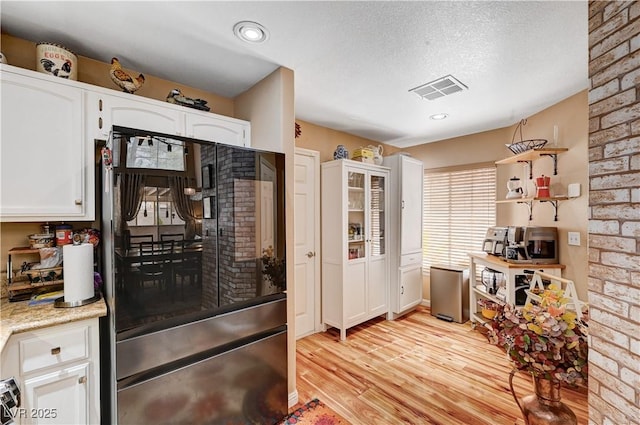 kitchen with visible vents, light wood-style flooring, a textured ceiling, white cabinetry, and fridge