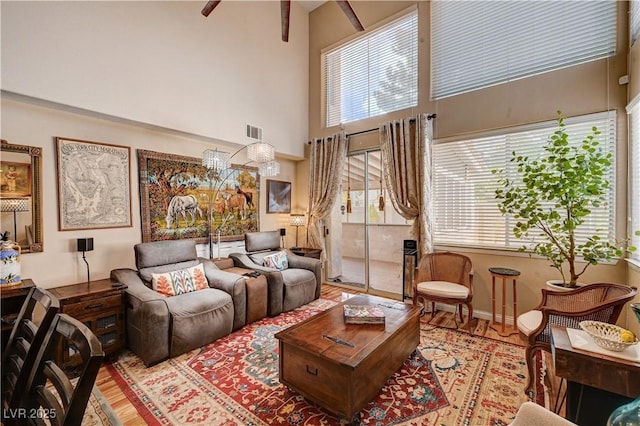 living area featuring visible vents, a towering ceiling, ceiling fan, and wood finished floors