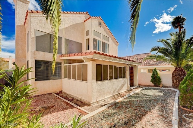 view of side of home with stucco siding, a sunroom, and a tiled roof