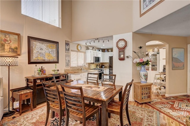 dining room featuring arched walkways, baseboards, light wood-type flooring, and a high ceiling