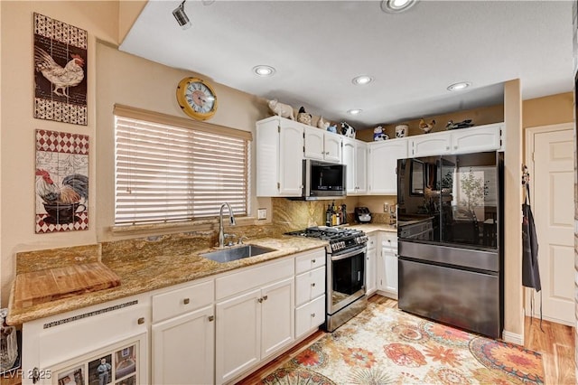 kitchen with a sink, light stone countertops, appliances with stainless steel finishes, and white cabinets