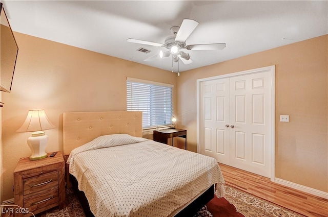 bedroom with wood finished floors, visible vents, baseboards, ceiling fan, and a closet