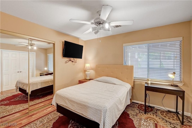 bedroom with visible vents, a ceiling fan, wood finished floors, a closet, and baseboards