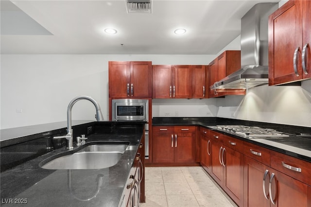 kitchen with visible vents, dark stone countertops, appliances with stainless steel finishes, wall chimney exhaust hood, and a sink