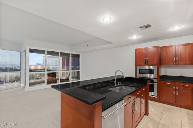 kitchen with visible vents, a center island with sink, a sink, dark stone counters, and appliances with stainless steel finishes