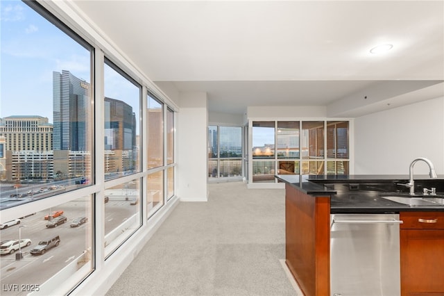 kitchen with brown cabinetry, a sink, stainless steel dishwasher, a view of city, and light colored carpet