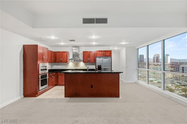 kitchen with dark countertops, visible vents, wall chimney range hood, built in appliances, and light colored carpet