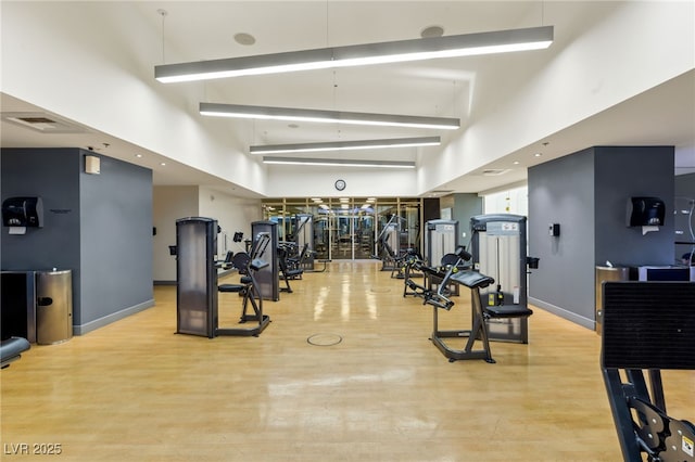 exercise room featuring visible vents, baseboards, a towering ceiling, and wood finished floors