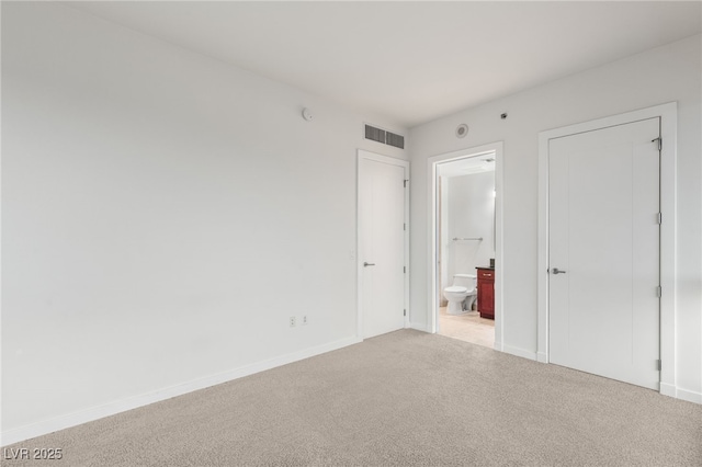 unfurnished bedroom featuring visible vents, baseboards, ensuite bathroom, and carpet